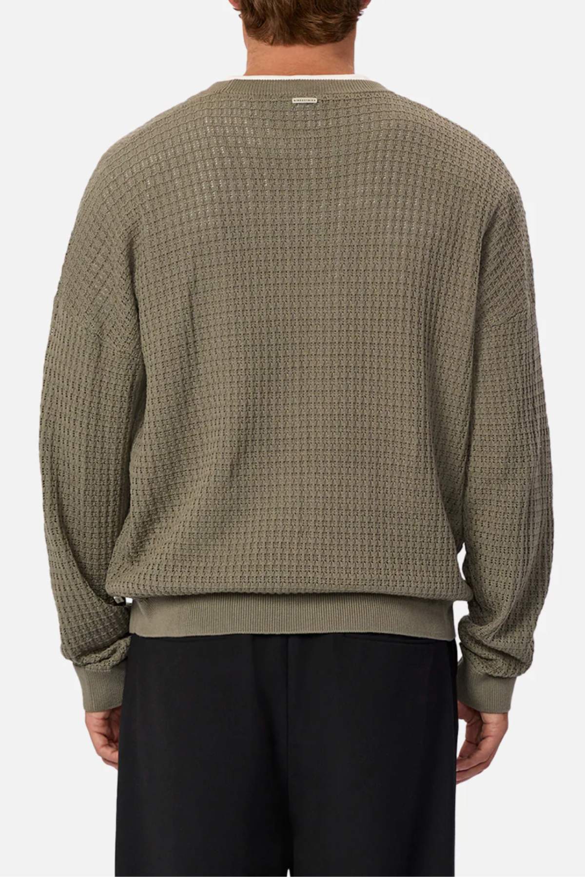 A person wears the Industrie The Nunez Long Sleeve Knit, an olive-green sweater with a woven pattern made of 100% cotton, featuring ribbed cuffs and hem. It's paired with black pants and set against a plain white background.