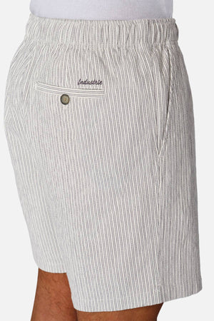A person models Industrie The Ortenza Short—light gray and white vertically striped men's cotton shorts with an elastic waistband, side pocket, and buttoned back pocket—shown from the side against a plain background.