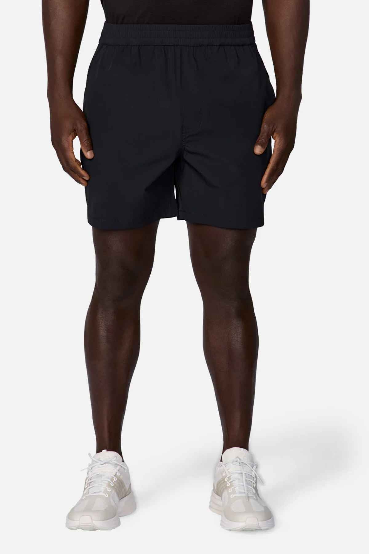 A person wearing a black T-shirt, Industrie The Owens Shorts featuring an elasticised waistband, and white sneakers stands against a plain white background. Only the lower part of their body is visible, showcasing the clothing and shoes.