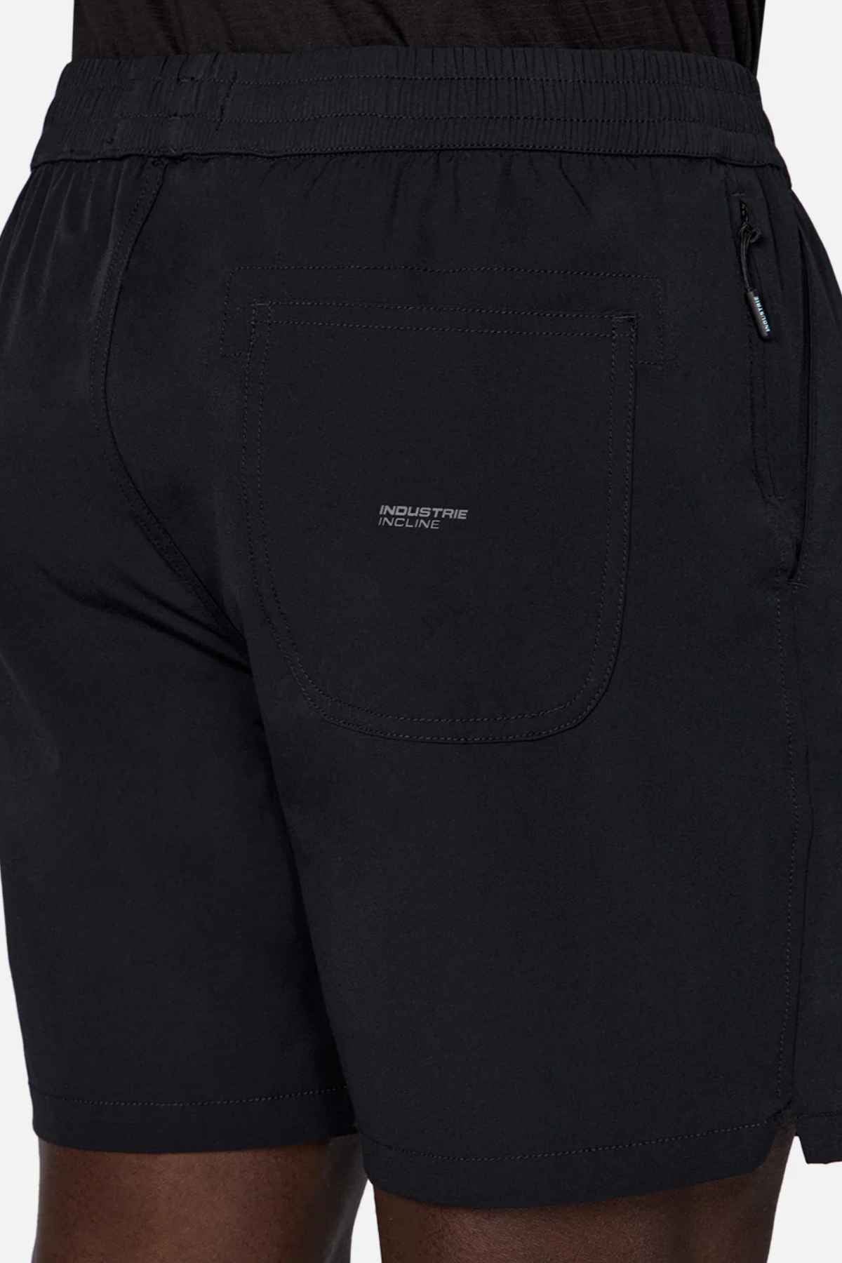 A person is wearing the trendy Industrie The Owens Short in black, featuring an elasticized waistband. These shorts are designed with a back pocket displaying the text "Industrie Incline" and have a small zipper pocket on the side. Made from quick-drying fabric, they're ideal against a plain white background.