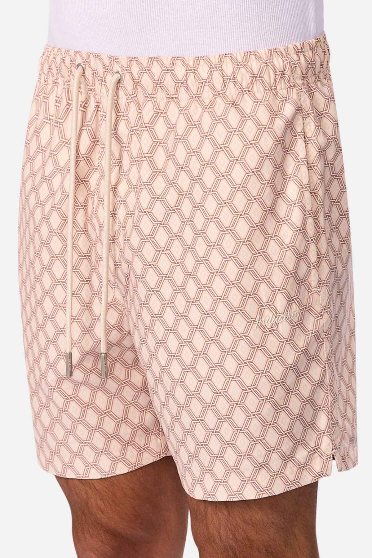 A person wearing Industrie The Panama Swim Short in light pink with a geometric hexagonal pattern, white drawstrings, and an elastic waistband—stylish men’s swimwear designed for quick-dry comfort.