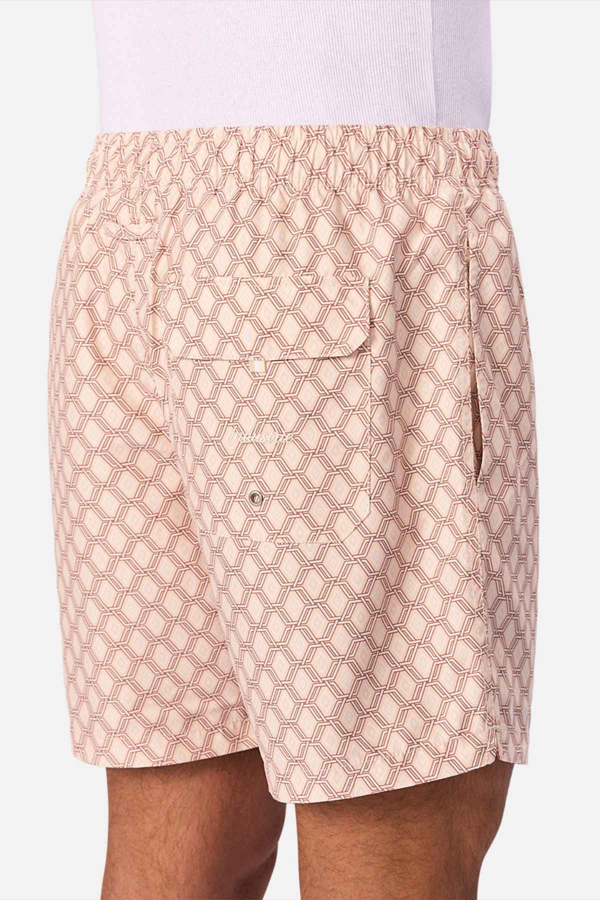 A person wears Industrie The Panama Swim Short in light pink with patterns, featuring an elastic waistband, back pocket with grommet, and side pocket. A white shirt is partly visible, highlighting these stylish men's swim shorts.