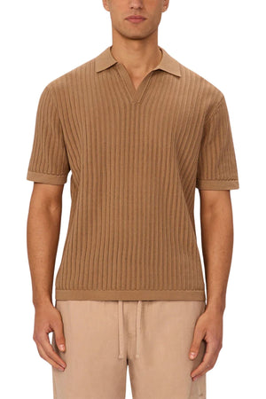 A man wears the Industrie The Poolside Polo, a short-sleeve ribbed tan cotton knit shirt with split neckline, paired with light beige drawstring pants. Its textured pattern and relaxed fit make it ideal for casual wear; his face is partly hidden.