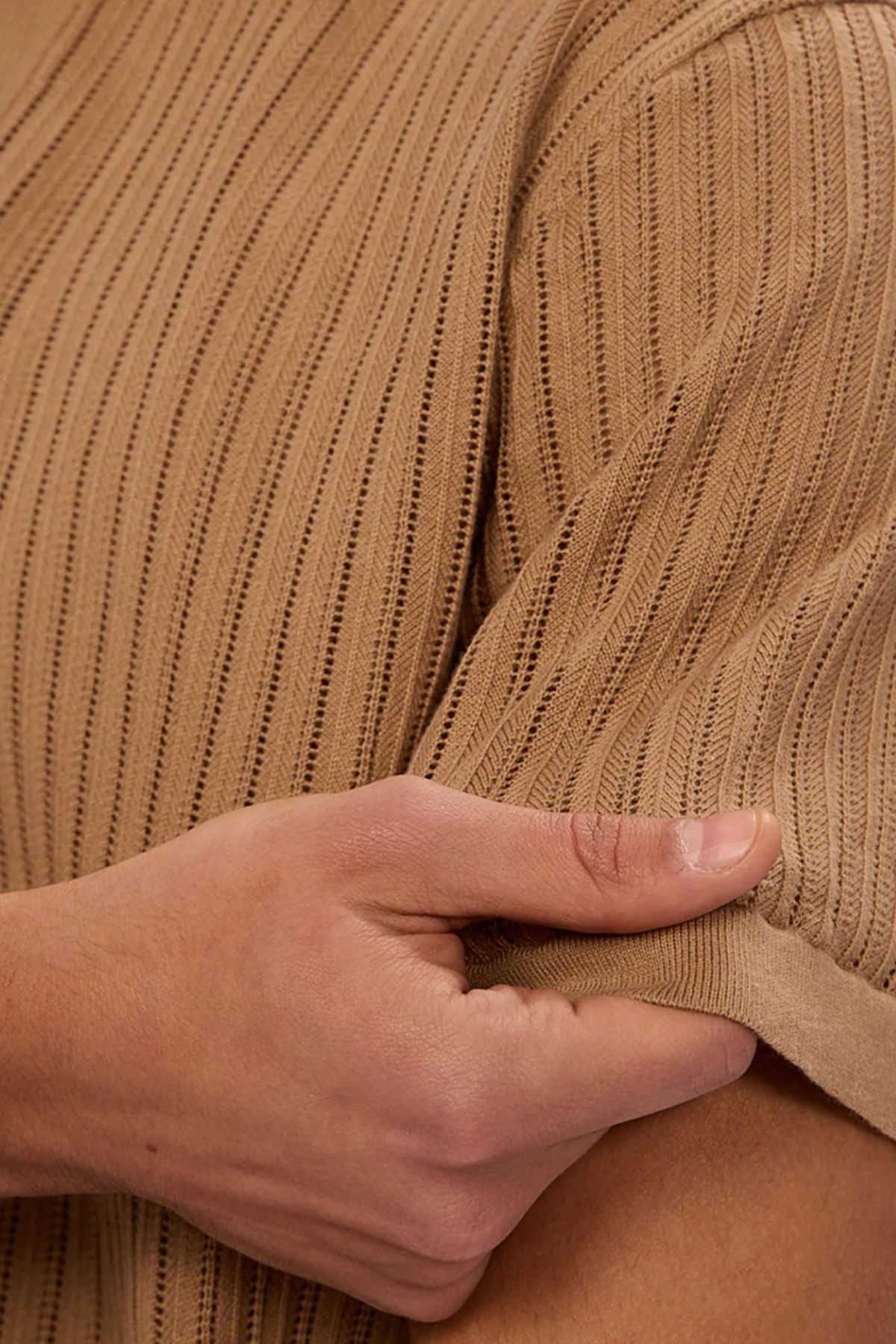 A close-up of a person holding the sleeve of the Industrie The Poolside Polo in light brown ribbed cotton knit, ideal for casual wear. The textured fabric and pattern are highlighted, showing only a hand, arm, and part of the upper body.