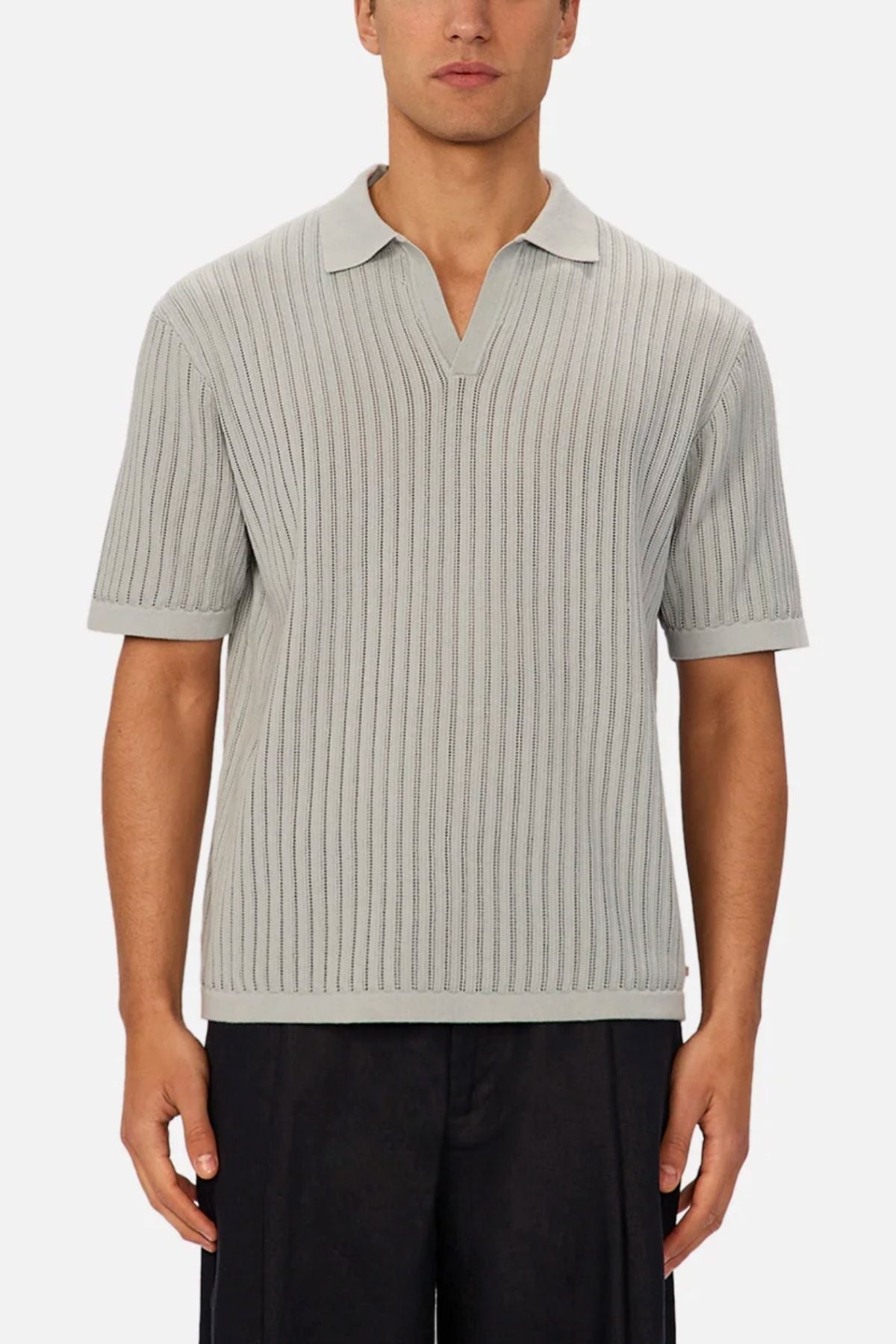A man in the light gray Industrie The Poolside Polo—a cotton knit collared shirt with a V-neck—paired with dark pants, stands against a plain background, making it ideal for casual wear.