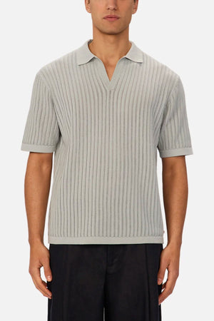 A man in the light gray Industrie The Poolside Polo—a cotton knit collared shirt with a V-neck—paired with dark pants, stands against a plain background, making it ideal for casual wear.