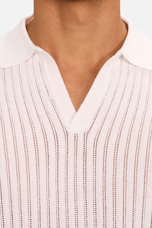 A close-up of a person wearing Industrie The Poolside Polo, a light pink cotton-knit with vertical textured stripes, V-neckline, and collar. Only the lower face and neck are visible, highlighting the casual style.