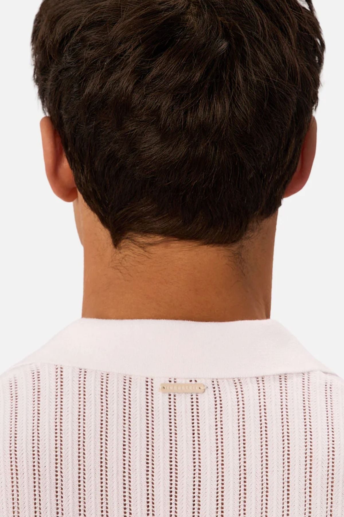 The back of a person’s head and neck with short brown hair. They wear the Industrie The Poolside Polo—white with vertical brown stripes and a small rectangular tag at the collar—ideal for casual style.