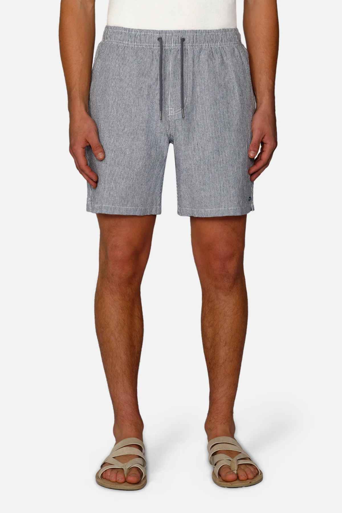 A person wearing Industrie The Portico Linen Short in gray, paired with a white top and beige sandals, stands against a white background. These shorts, perfect for a summer wardrobe, feature a drawstring waist. The focus remains on the lower half of the body.