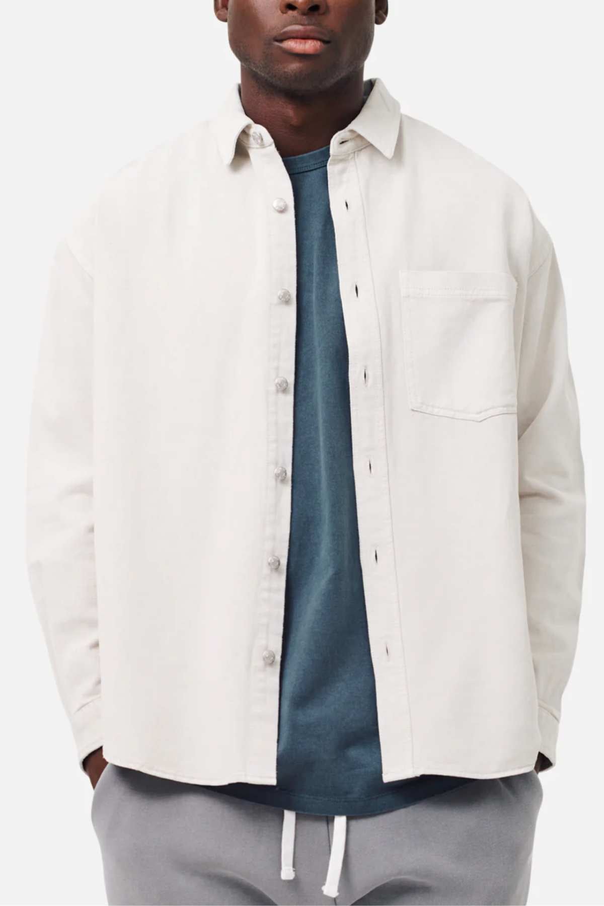A man wearing the Industrie The Portland Shirt, a relaxed fit white cotton linen overshirt, over a blue shirt with gray drawstring pants against a plain white background.