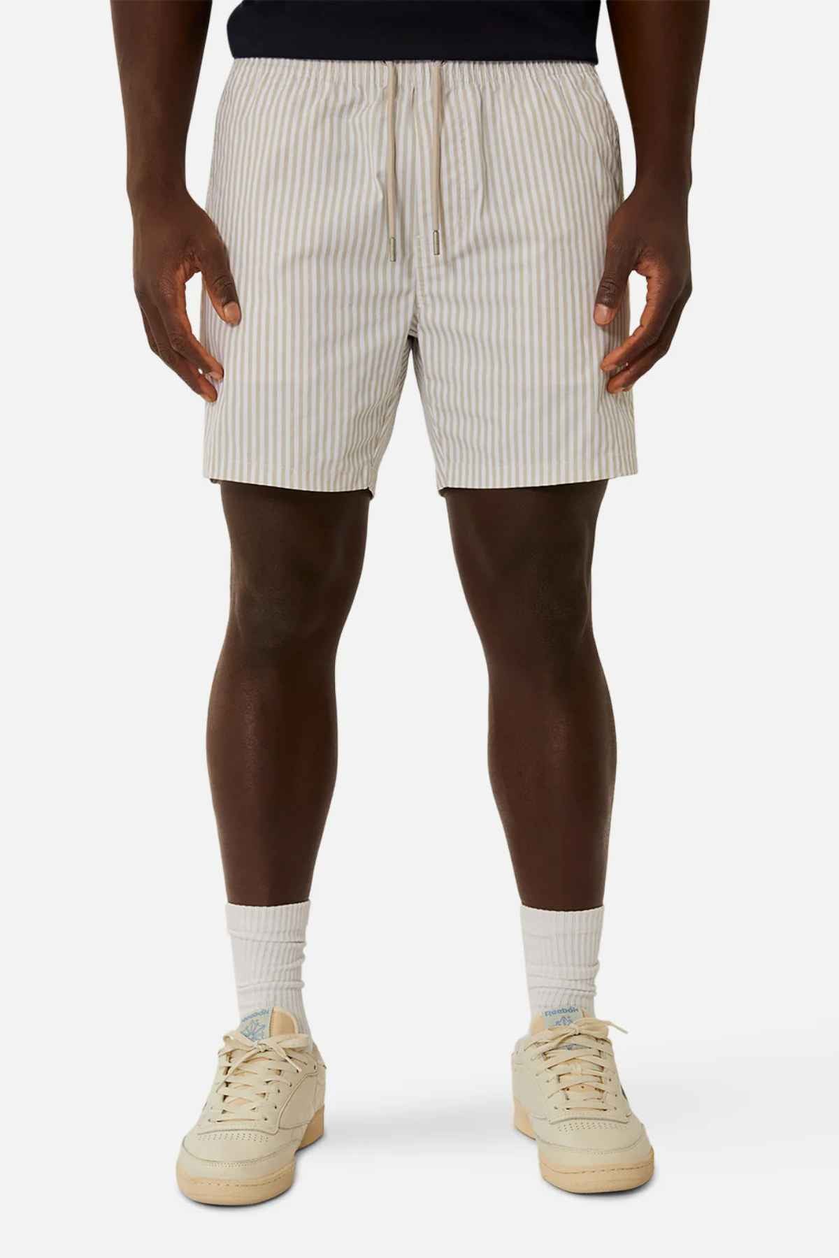 A person wearing the Industrie The Princeton Bahama Short with light-colored vertical stripes, paired with a black shirt, white socks, and beige sneakers. They stand effortlessly against a plain white background.