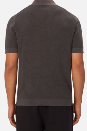 A person is shown from the back wearing the Industrie The Ravenna Polo in dark gray with a subtle waffle knit and straight hem, paired with black pants, set against a plain white background.