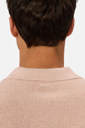 A person with short, dark hair is seen from behind wearing the Industrie The Ravenna Polo, a light pink textured waffle knit polo with a collar, set against a plain, light background.