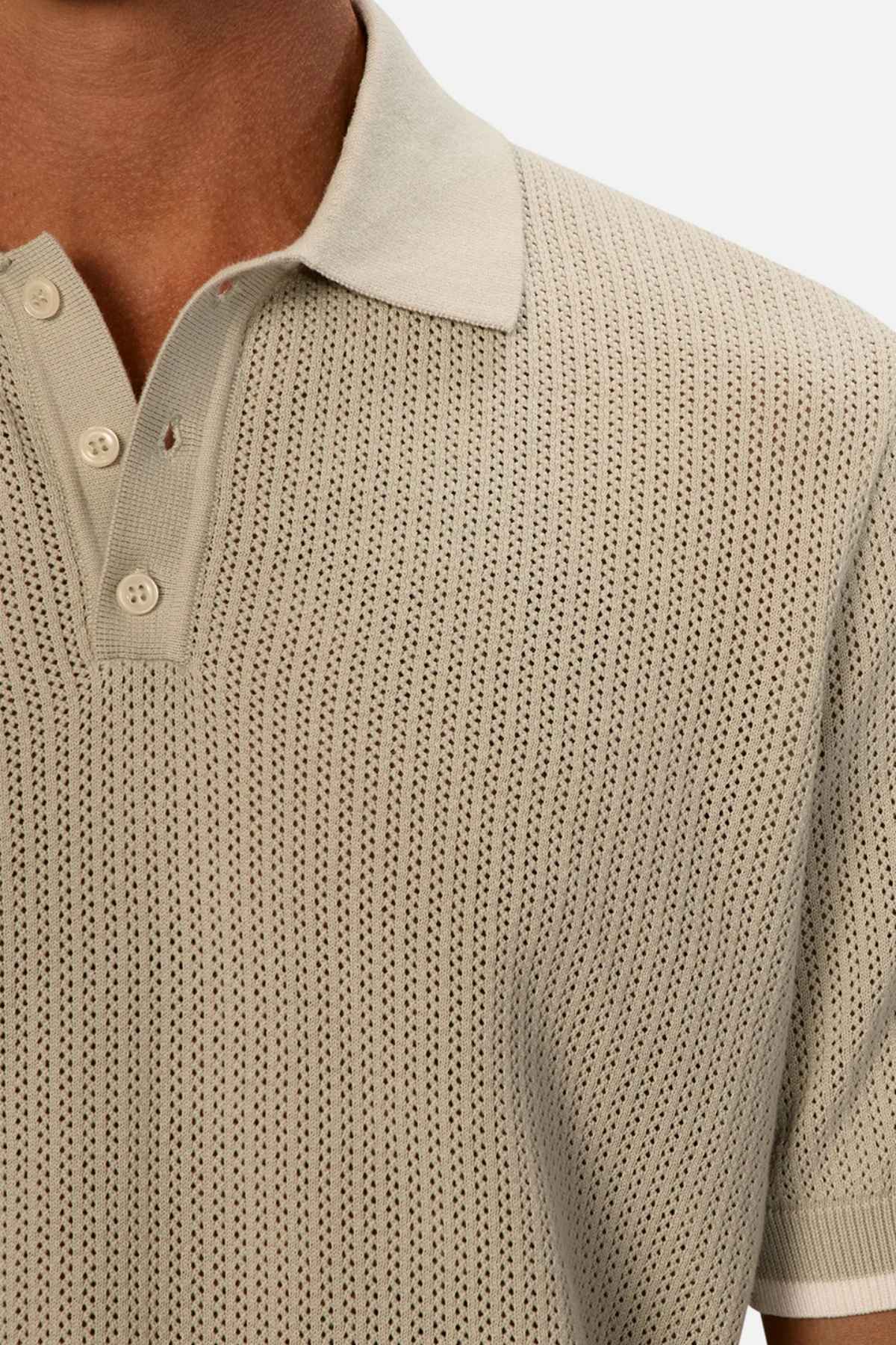Zoomed-in image of an individual dressed in Industrie The Serrano Polo, featuring its light green color and perforated patterned design. Made entirely from cotton, the textured polo is styled with the buttons undone, capturing just the shoulder and a portion of the chest against a neutral background.