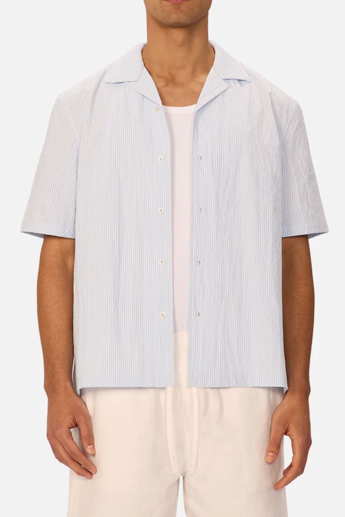A man wears the Industrie The Sorrento Short Sleeve Shirt in light blue and white pinstripes over a white tee with light pants. The image is cropped from just below his shoulders to above his knees.