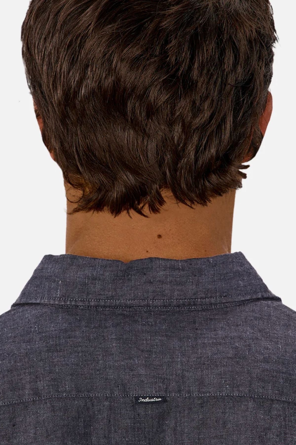 A person with short brown hair is shown from behind, wearing the Industrie The St Martins Shirt—a textured, dark blue regular-fit linen shirt with a small white embroidered label near the collar. The background is plain white.