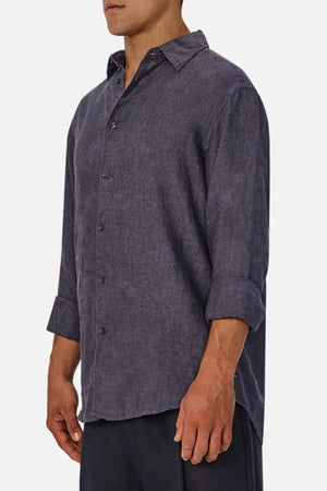 A man stands at a slight angle against a plain light background, wearing the Industrie The St Martins Shirt—a regular fit, long-sleeved dark grey linen shirt with rolled-up sleeves.
