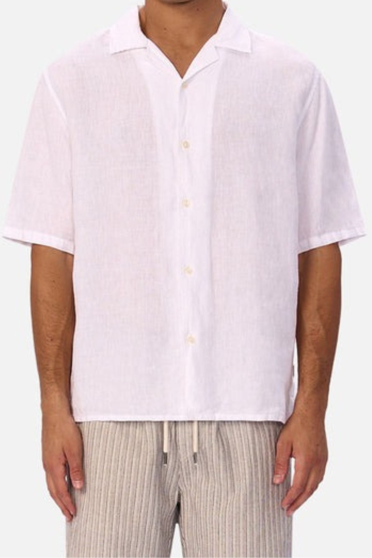 A person wears the Industrie The St Martins Short Sleeve Shirt paired with beige striped drawstring pants. The cropped image emphasizes the classic summer style of this men's collared, short sleeve linen shirt.