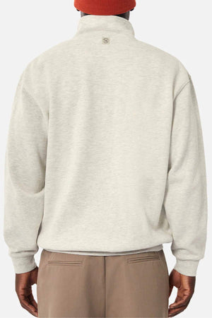 A person is shown from the back wearing the Industrie The Staunton Tracktop in light beige with fleece lining, paired with brown pants and a red beanie, all set against a plain white background.