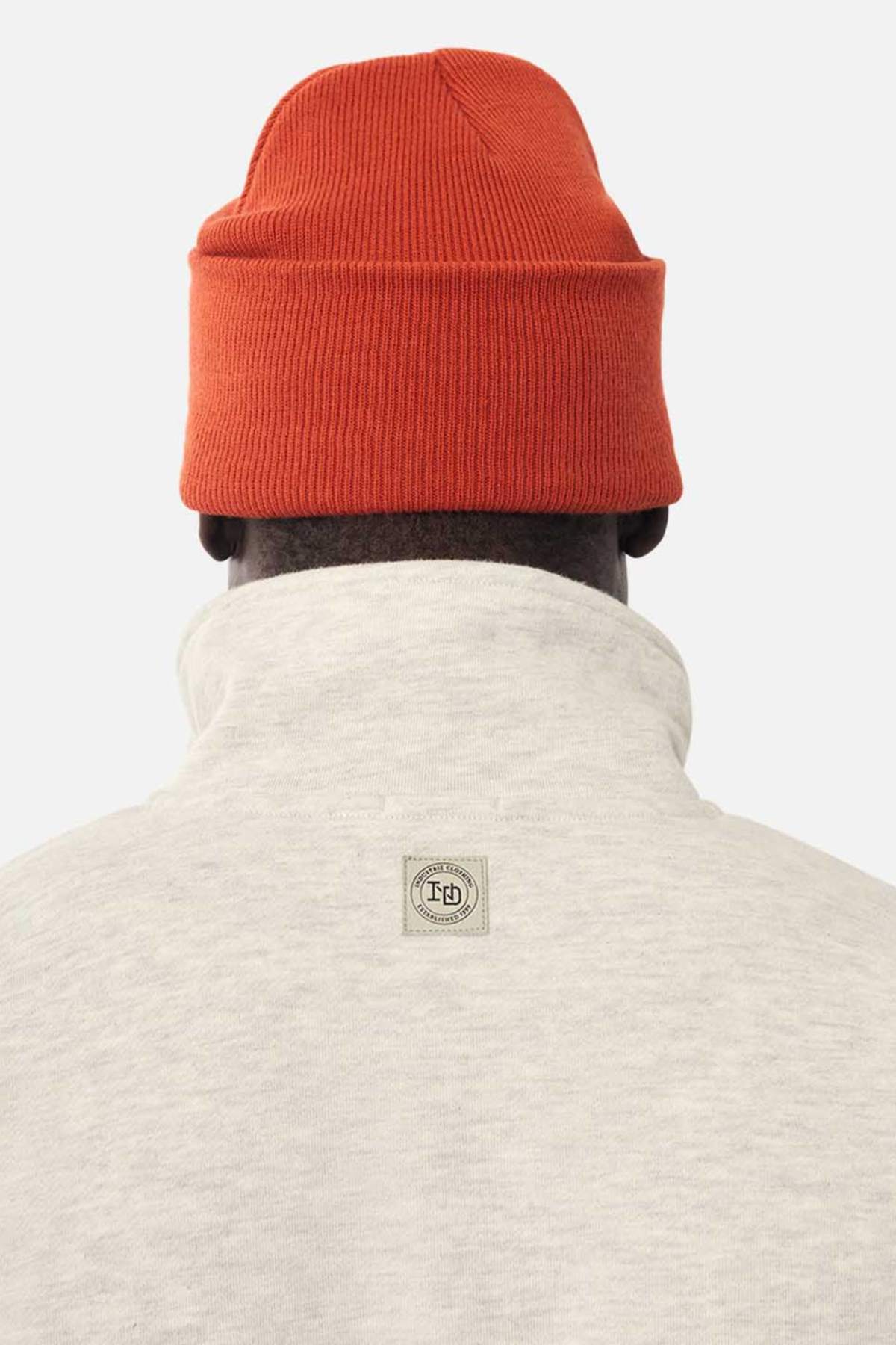 A person seen from behind wears a light gray Industrie The Staunton Tracktop with a high collar and small rectangular logo patch, paired with a bright orange knit beanie.
