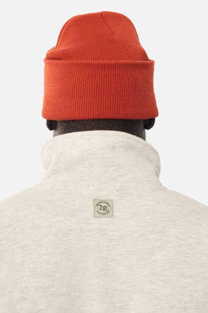 A person seen from behind wears a light gray Industrie The Staunton Tracktop with a high collar and small rectangular logo patch, paired with a bright orange knit beanie.