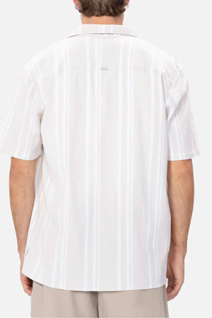 A person stands against a white background wearing the Industrie The Striped Magna Short Sleeve Shirt, featuring vertical stripes and a relaxed fit from breathable fabric, paired with beige pants.