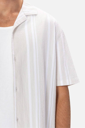 Close-up of someone in a white tank top beneath the Industrie The Striped Magna Short Sleeve Shirt, highlighting its loose fit and breathable fabric. The focus is on the upper torso and shoulder area against a plain background.