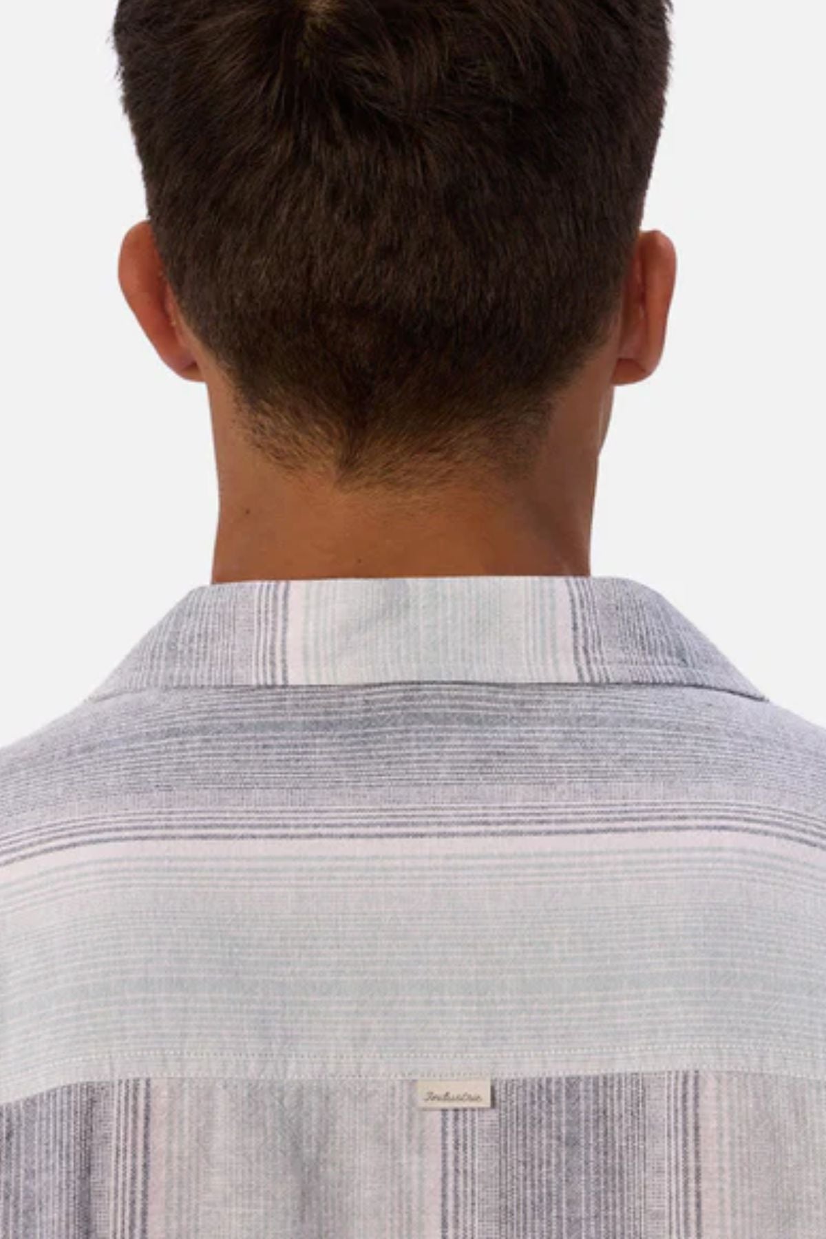 A person with short brown hair is seen from behind, wearing the Industrie The Sunset Short Sleeve Shirt, which features light-colored stripes. The background is plain and light gray.
