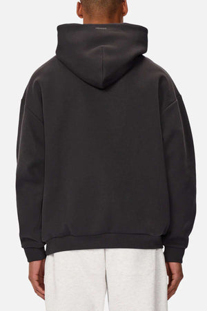 A person is seen from the back wearing Industrie The Tech Del Sur Hood in black, crafted with advanced athletic fabrications, paired with light gray pants. It features a slightly oversized fit and a small logo at the top on a plain white background.