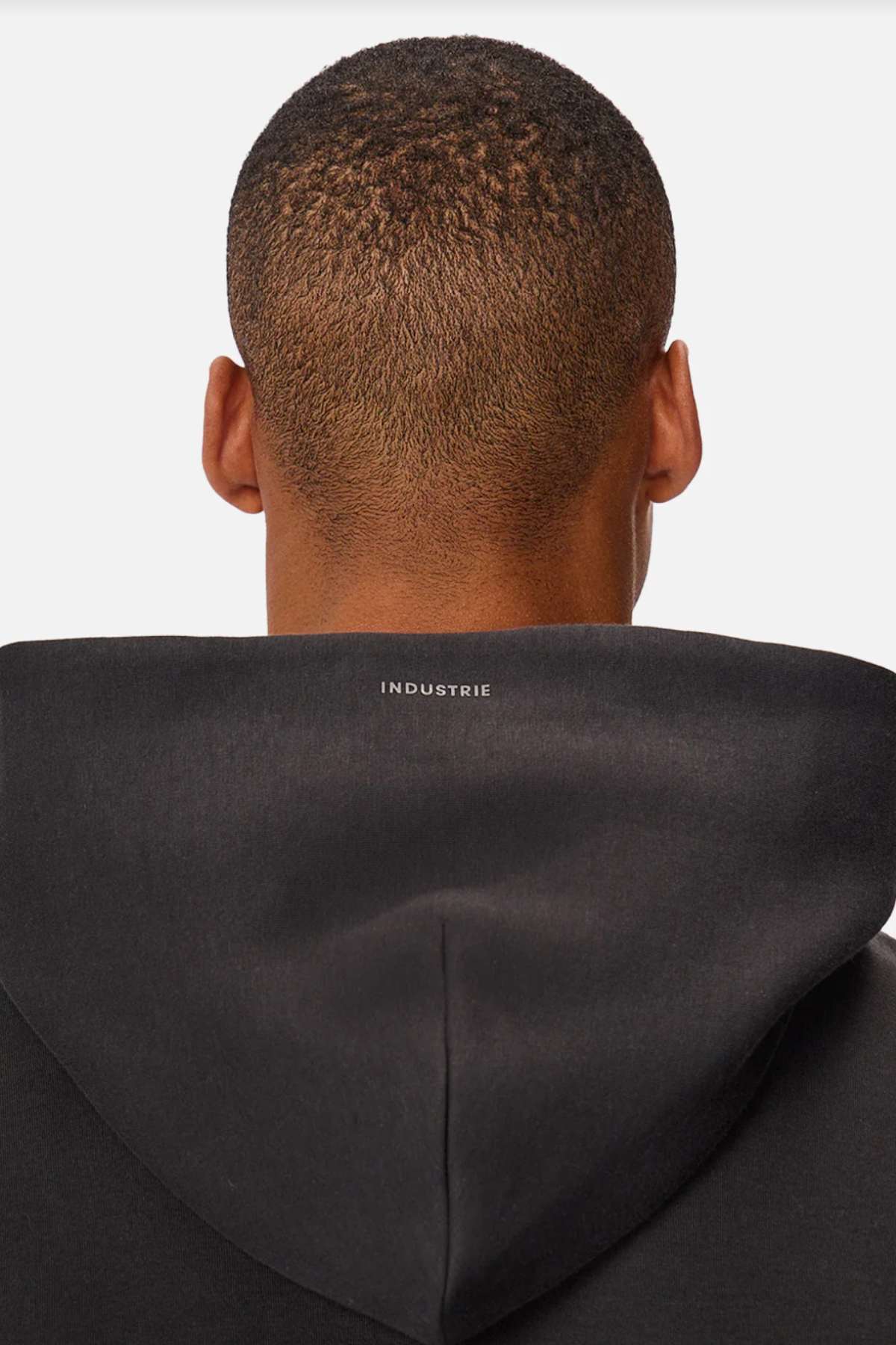 A person wearing the Industrie The Tech Del Sur Hood, featuring "INDUSTRIE" on the back, made from advanced athletic fabrics for a modern yet stylish look, seen from behind against a white background.