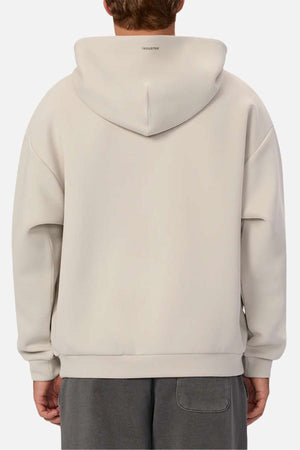 A person is seen from the back in an Industrie The Tech Del Sur Hood sweatshirt in light beige, featuring the INDUSTRIE logo on the upper back. The hood rests down, paired with dark gray athletic-style pants.