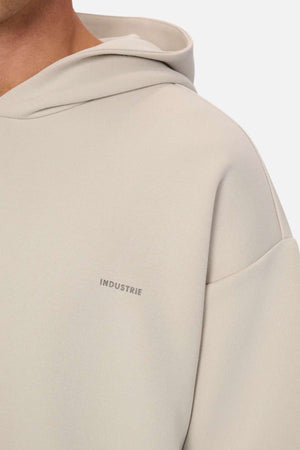 A close-up of the Industrie The Tech Del Sur Hood, a light beige sweatshirt with a small gray INDUSTRIE logo on the left chest. Only the upper chest and shoulder are shown, highlighting its athletic fabric.