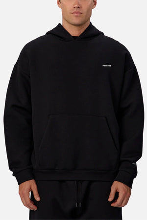 Someone wears the Industrie The Tech Del Sur Hoodie—plain black with a small white logo on the left chest. This athletic hoodie has a front pocket, loose fit, and is shown against a light gray background.