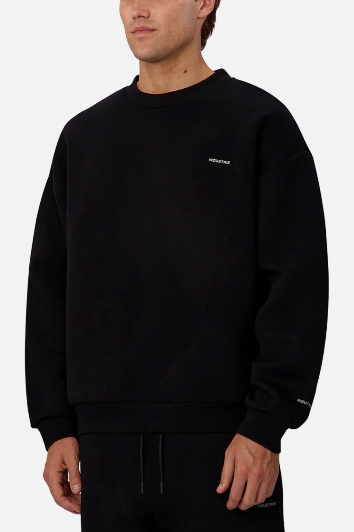 A person models the Industrie The Tech Del Sur Sweat, featuring subtle white text on the left chest and wrist, paired with matching black pants against a plain background.