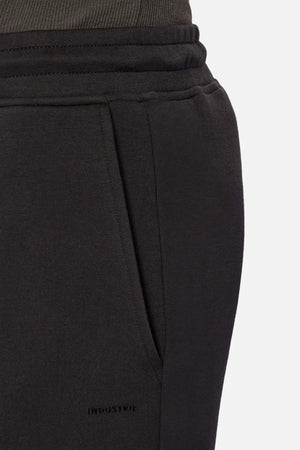 Close-up of a person wearing Industrie The Tech Del Sur Track Pant in black jogger style with an elastic waistband, side pocket, and subtle stitching detail. Made from athletic material for superior comfort and performance.