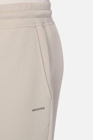 Close-up of a light beige pair of Industrie The Tech Del Sur Track Pant with an elastic waistband and a visible pocket on the right side. The brand name "INDUSTRIE" is printed just below the pocket. The fabric appears soft and comfortable, suggesting casual wear.