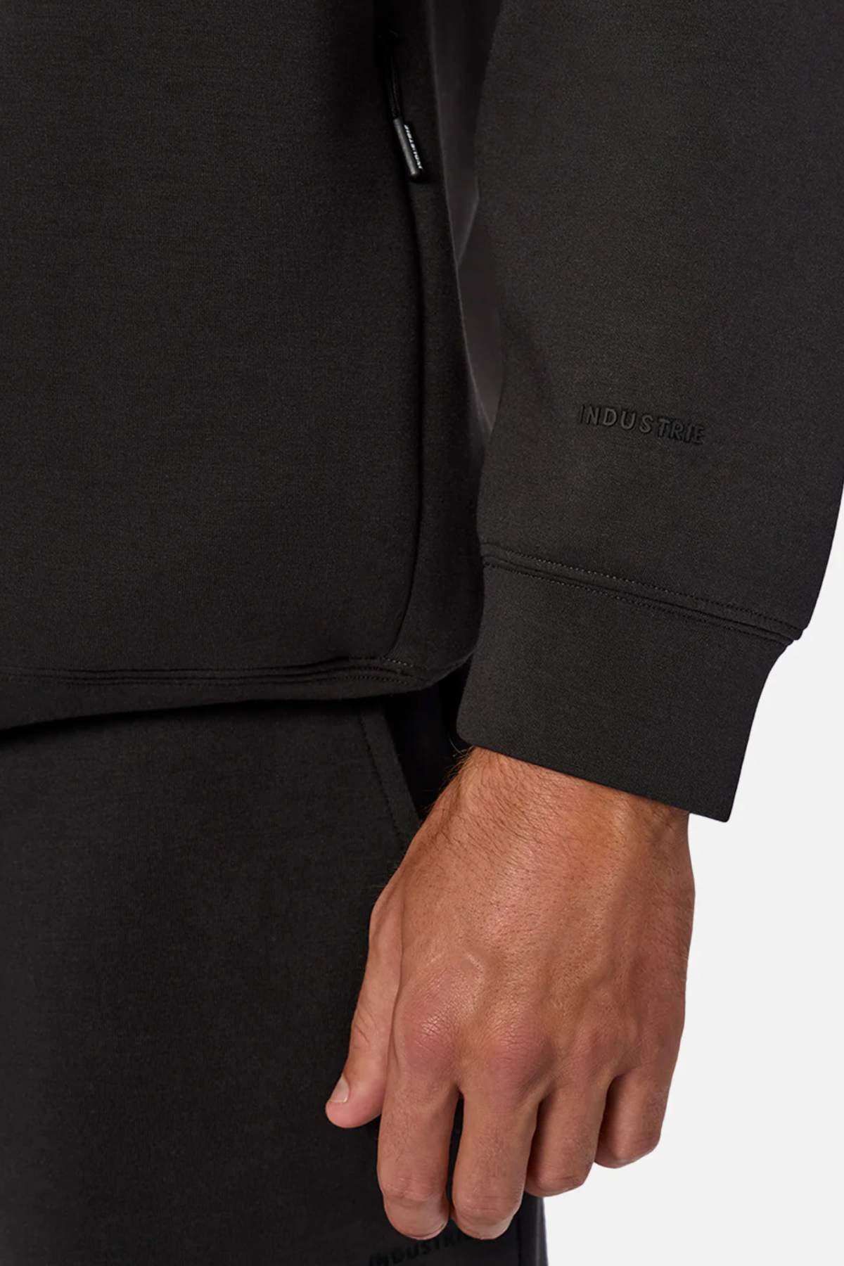 A close-up of a hand wearing the Industrie The Tech Staunton Track Top, featuring “INDUSTRIE” embroidered near the wrist and a zippered pocket, all crafted from athletic fabric.