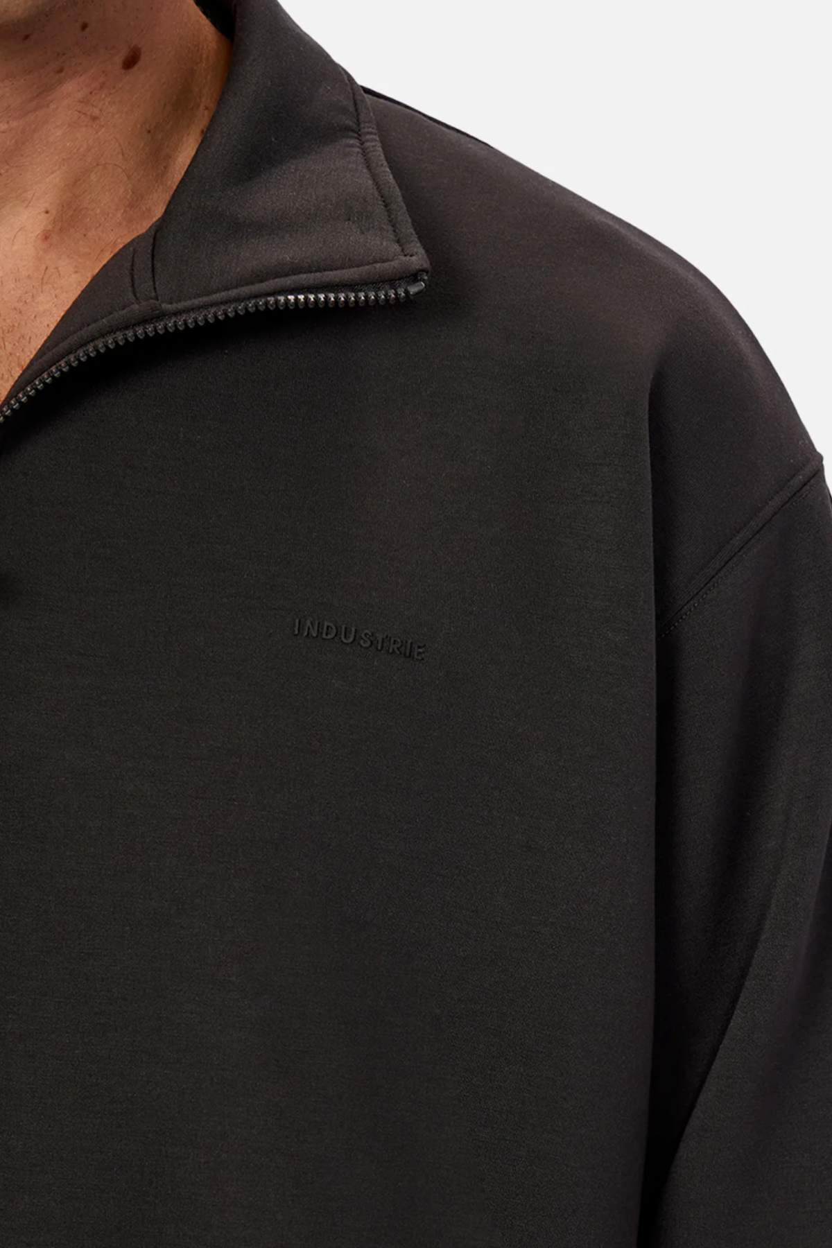 Close-up of a person wearing the Industrie The Tech Staunton Track Top in black, with "INDUSTRIE" subtly embroidered on the chest. Only part of their neck and shoulder is visible, emphasizing the sleek athletic fabric.