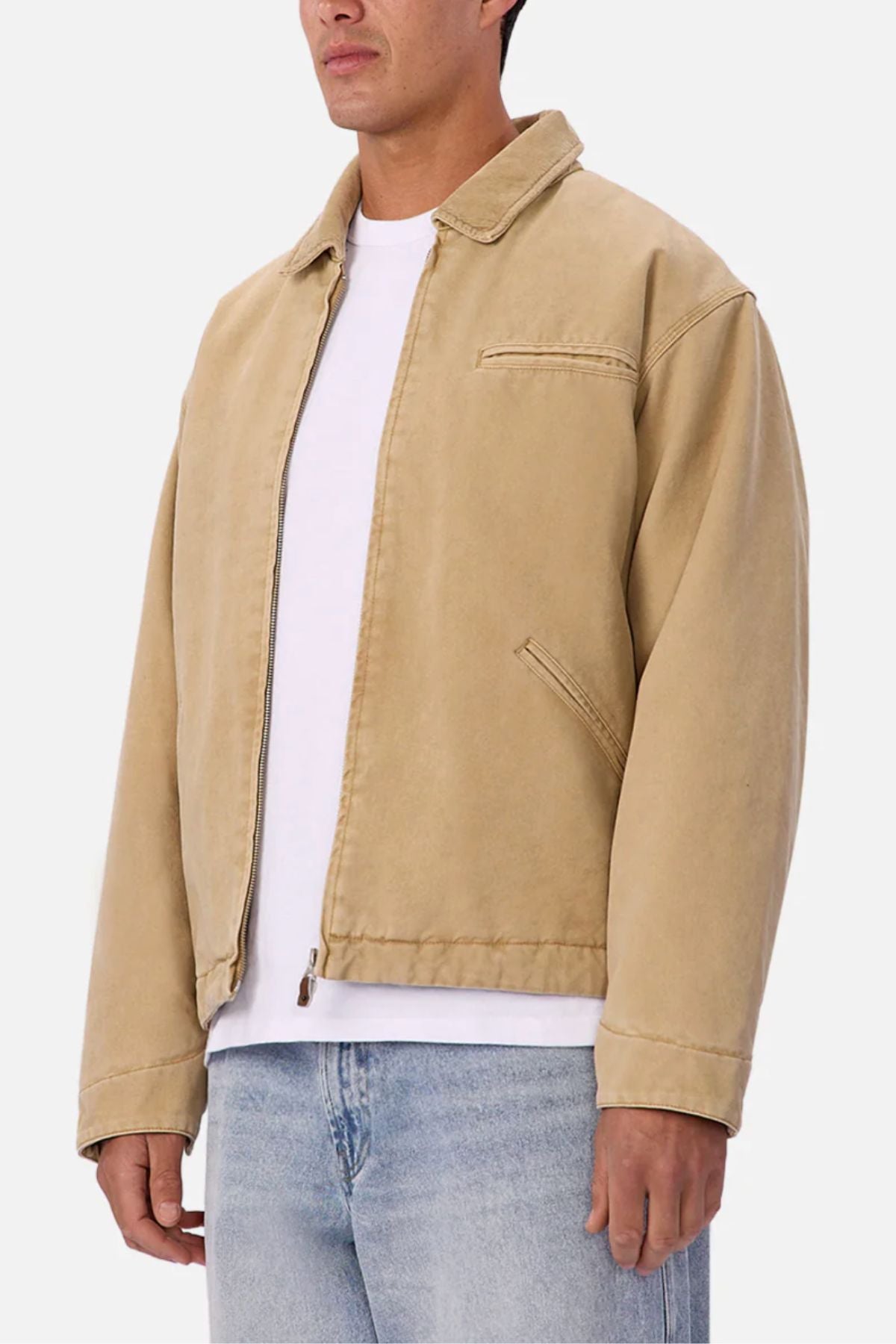 A person wearing the Industrie The Tennesse Jacket—a beige zip-up men's casual jacket made of 100% cotton—over a white t-shirt and light blue jeans, standing against a plain white background.