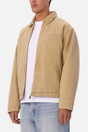 A person wearing the Industrie The Tennesse Jacket—a beige zip-up men's casual jacket made of 100% cotton—over a white t-shirt and light blue jeans, standing against a plain white background.