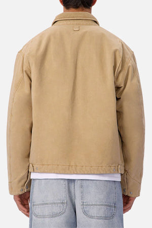 A person with short dark hair is seen from the back wearing the Industrie The Tennesse Jacket, a 100% cotton men’s casual beige waist-length jacket with visible stitching and metal waistband buttons, paired with light blue denim jeans.