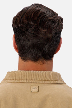 A person with short, wavy dark brown hair is seen from behind wearing the Industrie The Tennesse Jacket—a men's casual tan 100% cotton corduroy jacket with a small rectangular label at the collar. The background is plain white.
