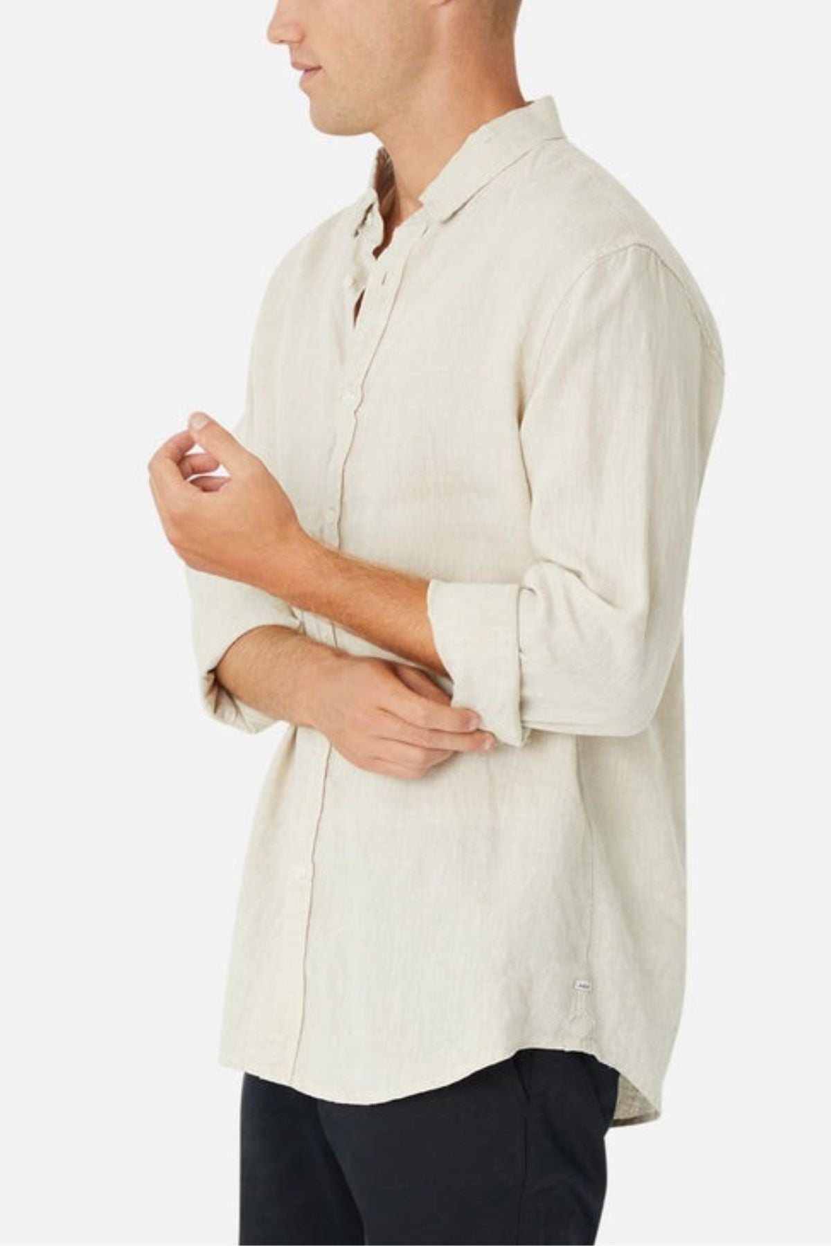 Wearing the Industrie The Tennyson Linen Blend Shirt in a light hue, with its spread collar and rolled-up sleeves, someone pairs it stylishly with black pants. They stand against a plain white background, slightly turned to the side, adjusting their sleeve—a perfect look for summertime.