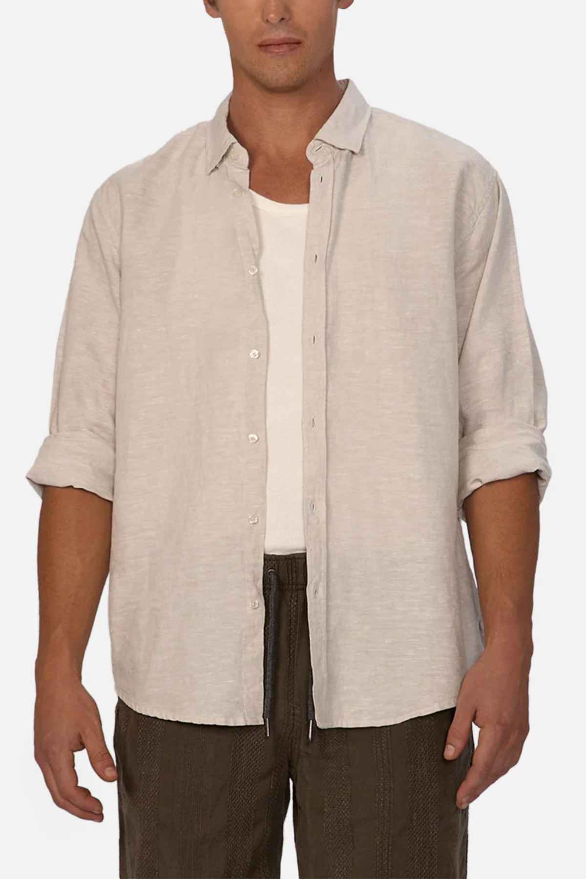 A person wearing the Industrie The Tennyson Linen Blend Shirt in beige over a white tank top and dark pants. The shirt features a spread collar and long sleeves, which are partially rolled up. The image emphasizes this summertime attire, set against a plain white background.