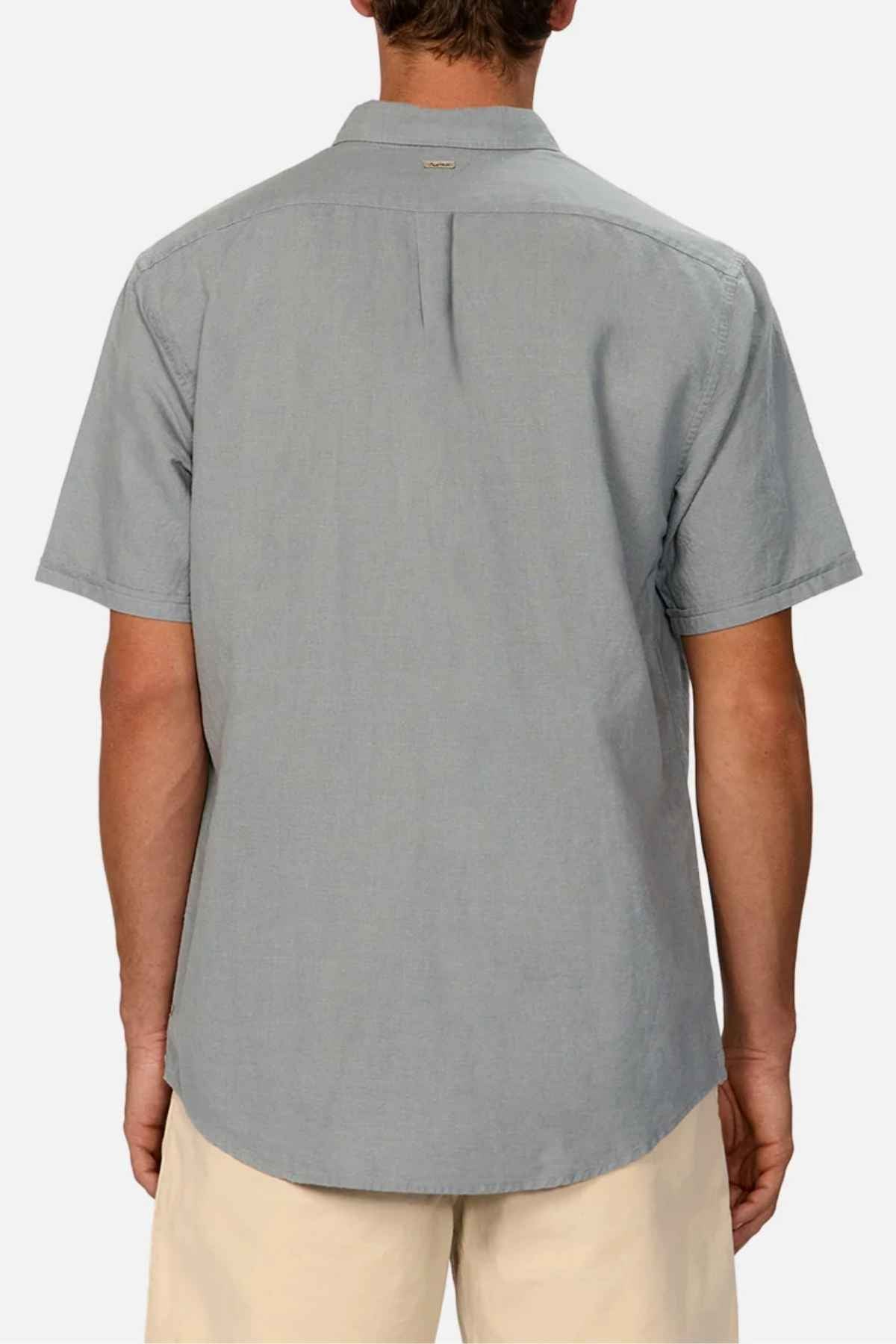 An individual in the Industrie The Tennyson Linen Blend Short Sleeve Shirt, showcasing its versatile light gray hue and straight hem, is photographed with their back to the camera. They pair it with light beige pants, capturing a sense of summertime comfort against a plain white backdrop.