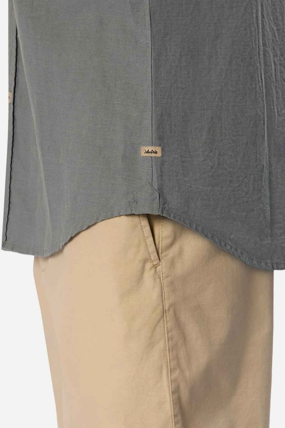 Close-up of a person wearing the Industrie The Tennyson Linen Blend Short Sleeve Shirt in gray, paired with beige pants. The shirt has a small tag on the side seam near the hem. The pants feature a visible pocket, enhancing their summertime comfort against a plain white background.