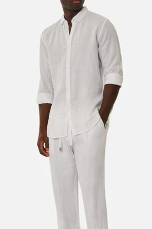 A man wearing the Industrie The Tennyson Linen Blend Shirt in white, sleeves rolled up, paired with matching white linen pants and standing with one hand in his pocket against a plain background.