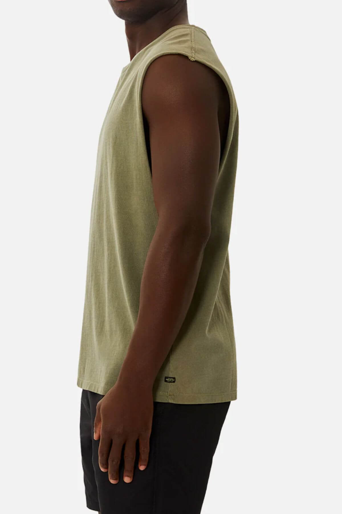A person stands in an olive green Industrie The Triple G Sleeveless Tee, made from 100% cotton, paired with black shorts. Photographed against a plain backdrop, they face left in the iconic style of the brand.