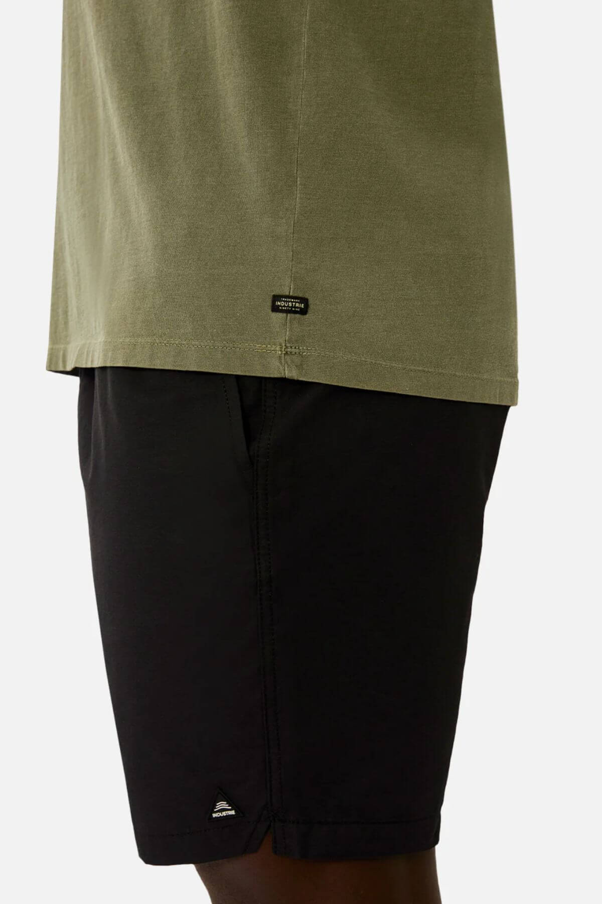 A person wears the Industrie The Triple G Sleeveless Tee, 100% cotton, in a casual outfit paired with black shorts. The image shows a partial side view on a plain white background.