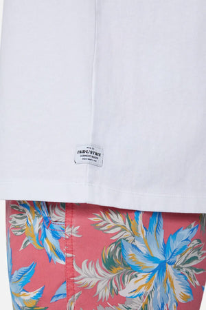 Close-up of the white "Industrie The Triple G Sleeveless Tee," made from 100% cotton, paired with relaxed-fit pink shorts featuring a vibrant blue, white, and yellow floral pattern. A small "Industrie" label is near the hem.